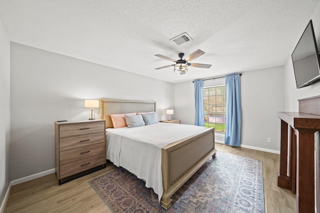 bedroom with baseboards, visible vents, a ceiling fan, a textured ceiling, and light wood-style floors