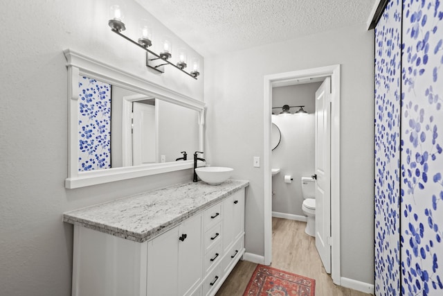 bathroom featuring baseboards, toilet, wood finished floors, a textured ceiling, and vanity