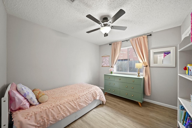 bedroom with a ceiling fan, baseboards, a textured ceiling, and light wood finished floors