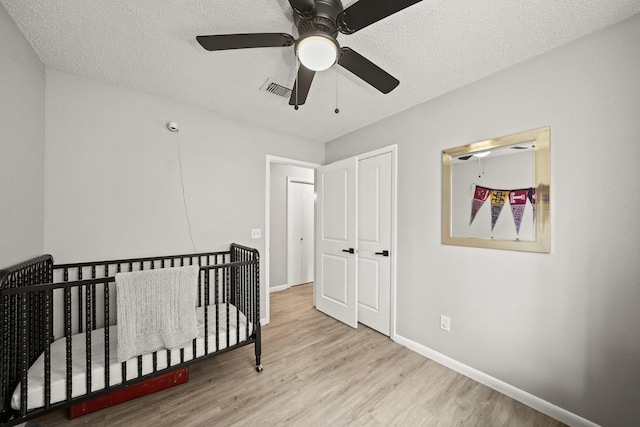 bedroom featuring baseboards, a textured ceiling, visible vents, and wood finished floors