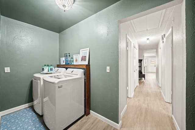 laundry room featuring a textured wall, light wood-style flooring, separate washer and dryer, baseboards, and attic access