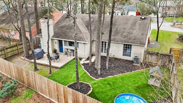 rear view of house with brick siding, a chimney, a wooden deck, and a fenced backyard