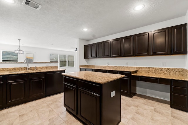 kitchen with black dishwasher, visible vents, a sink, light stone countertops, and built in desk