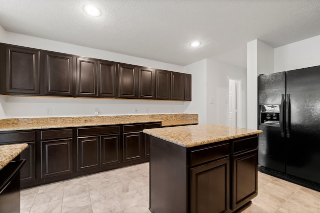 kitchen featuring light stone countertops, recessed lighting, dark brown cabinets, a center island, and black refrigerator with ice dispenser