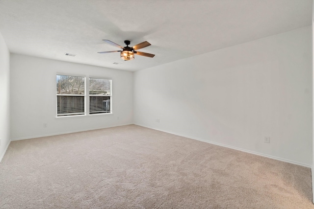 spare room featuring light carpet, ceiling fan, visible vents, and baseboards