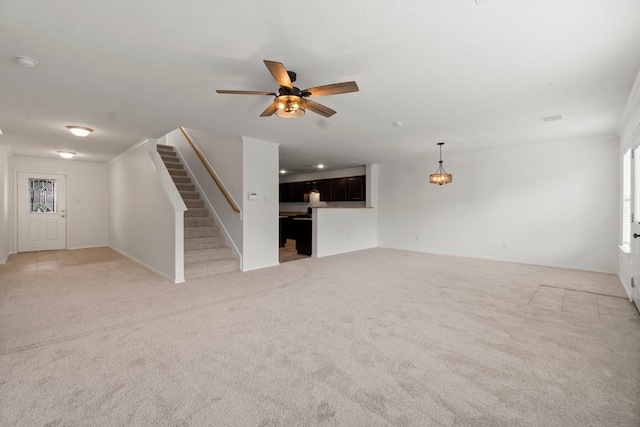 unfurnished living room featuring ceiling fan, stairs, and light colored carpet