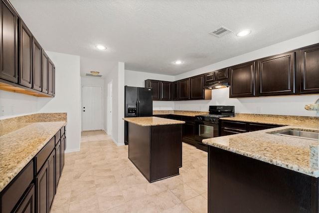 kitchen with visible vents, light stone counters, under cabinet range hood, black appliances, and a sink