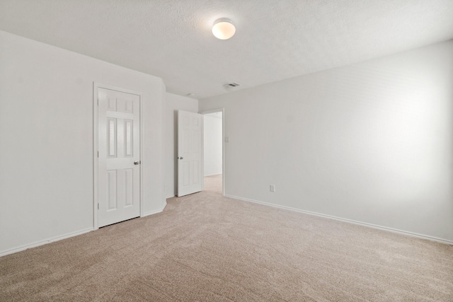 empty room with baseboards, visible vents, light carpet, and a textured ceiling