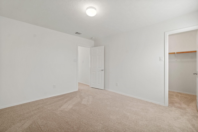 unfurnished bedroom with a walk in closet, a closet, light colored carpet, visible vents, and baseboards