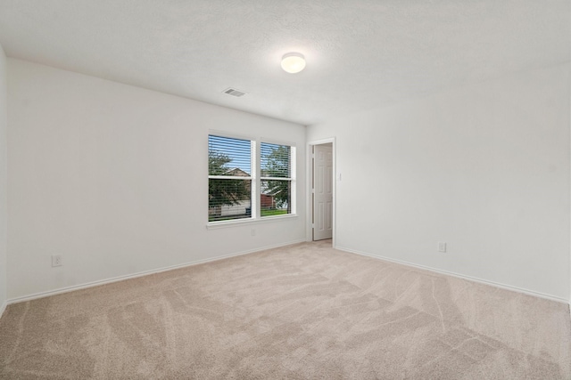 spare room with light colored carpet, visible vents, a textured ceiling, and baseboards