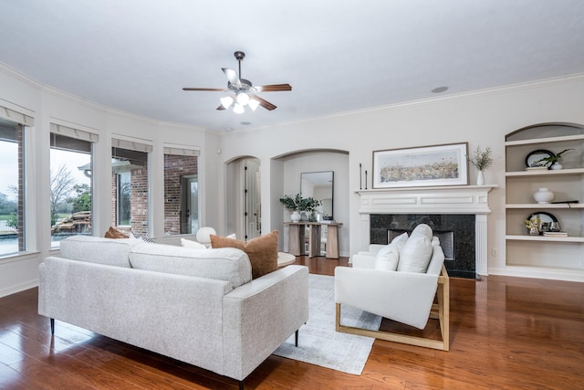 living area featuring arched walkways, built in shelves, wood finished floors, and a high end fireplace