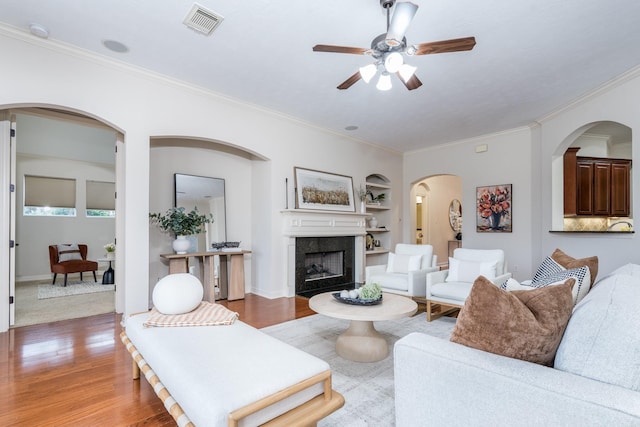 living room featuring built in features, crown molding, visible vents, a premium fireplace, and wood finished floors