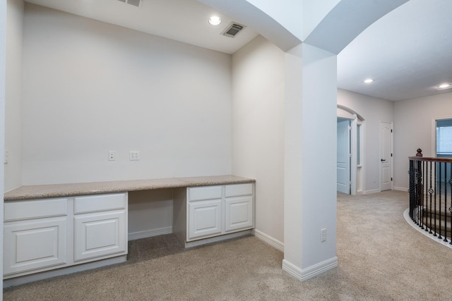 unfurnished office featuring baseboards, visible vents, arched walkways, light colored carpet, and built in desk