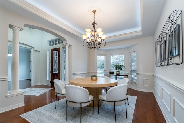 dining room featuring a tray ceiling, arched walkways, decorative columns, dark wood-type flooring, and a chandelier