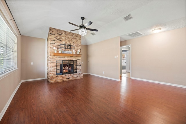 unfurnished living room featuring lofted ceiling, a brick fireplace, wood finished floors, and visible vents