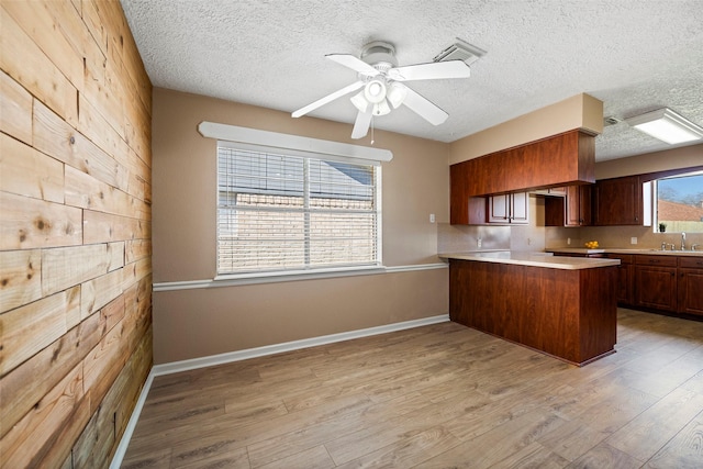 kitchen featuring light wood finished floors, visible vents, light countertops, a sink, and a peninsula