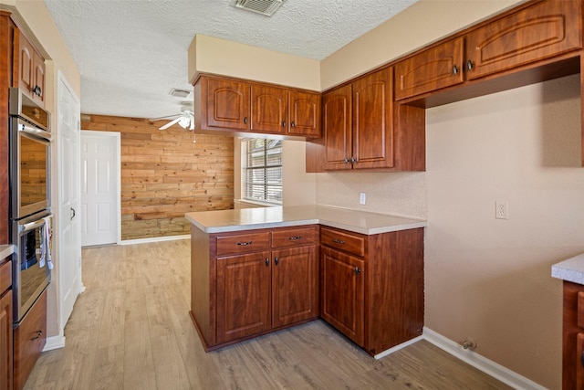 kitchen featuring ceiling fan, a peninsula, light countertops, light wood-type flooring, and brown cabinets