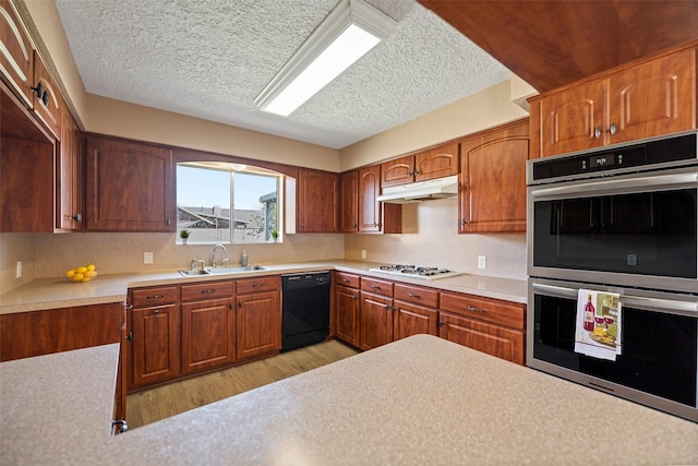 kitchen with black dishwasher, light countertops, stainless steel double oven, under cabinet range hood, and a sink