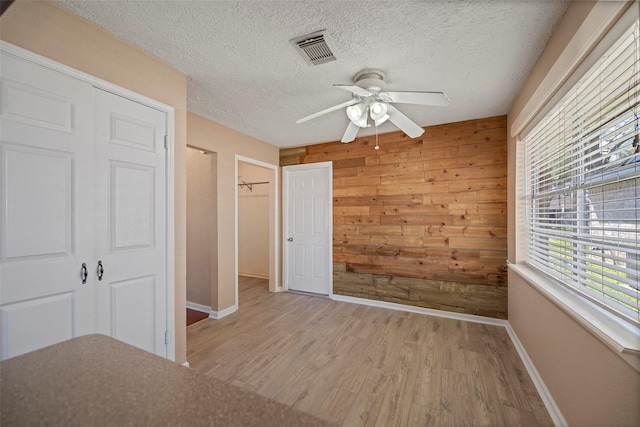 unfurnished bedroom featuring a textured ceiling, light wood-style flooring, wooden walls, visible vents, and a closet