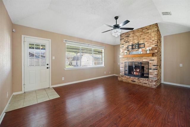 unfurnished living room featuring a brick fireplace, vaulted ceiling, a textured ceiling, and wood finished floors