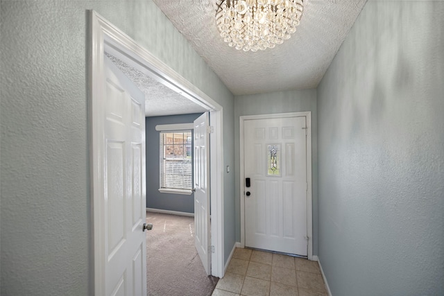 doorway featuring a textured ceiling, a textured wall, light carpet, baseboards, and an inviting chandelier