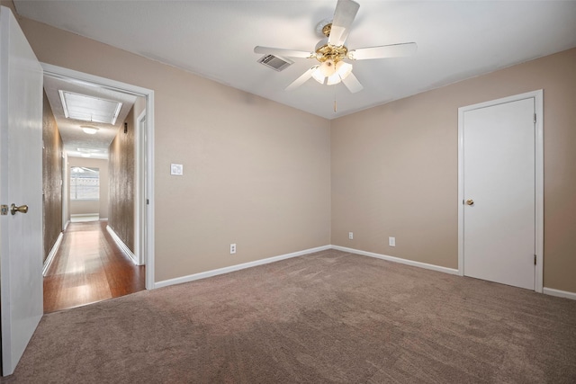 unfurnished room with carpet flooring, visible vents, baseboards, a ceiling fan, and attic access