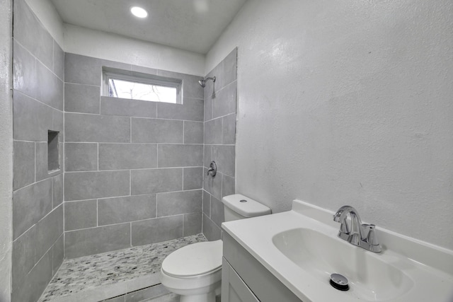 bathroom featuring vanity, toilet, a textured wall, and a tile shower