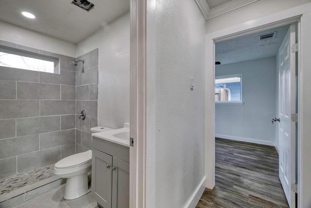 full bath with vanity, wood finished floors, visible vents, tiled shower, and toilet