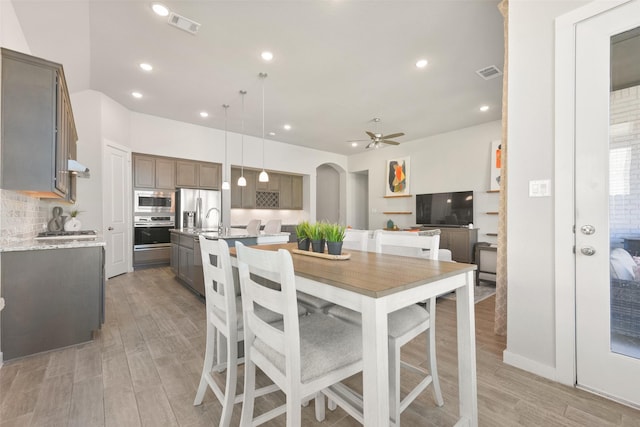 dining area featuring arched walkways, ceiling fan, visible vents, and light wood-style floors