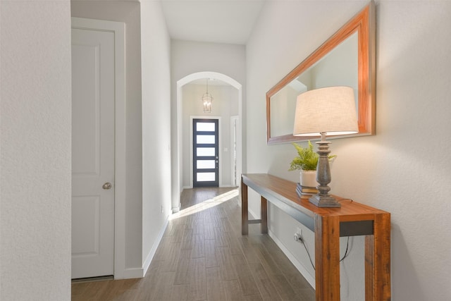 entryway with arched walkways, baseboards, and wood finished floors