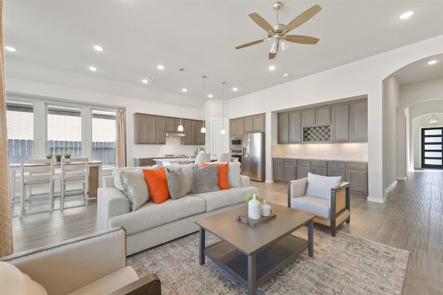 living area with arched walkways, ceiling fan, light wood finished floors, and a healthy amount of sunlight