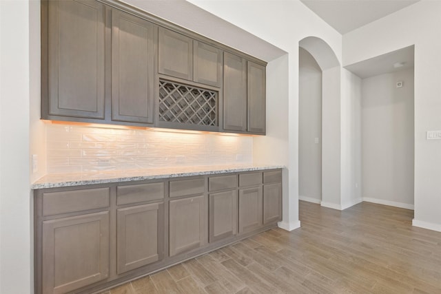 kitchen with baseboards, arched walkways, light stone counters, light wood-style floors, and backsplash