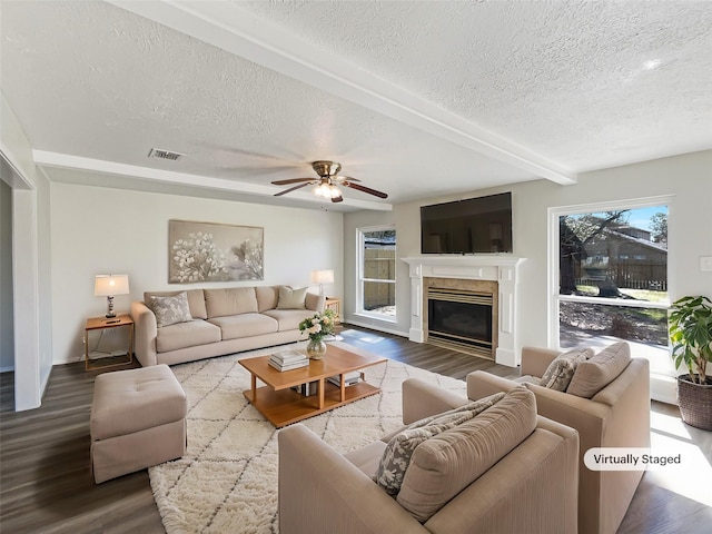 living area featuring a glass covered fireplace, ceiling fan, a textured ceiling, and wood finished floors