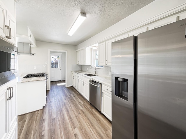 kitchen with light wood finished floors, white cabinetry, stainless steel appliances, and a sink