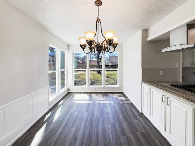 unfurnished dining area with dark wood-type flooring, a chandelier, wainscoting, and a textured ceiling