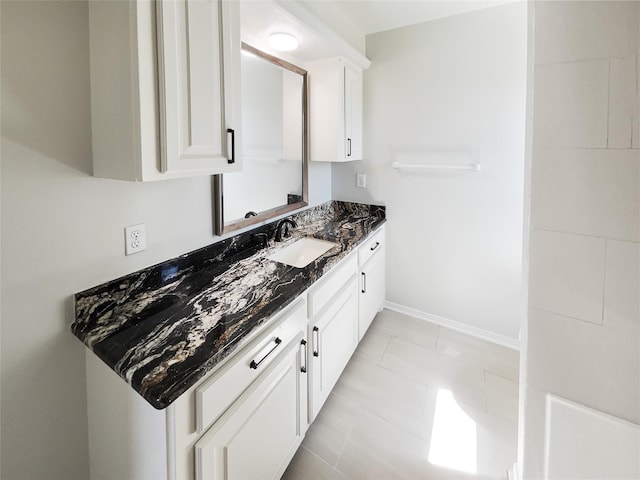 kitchen with baseboards, dark stone countertops, white cabinetry, and a sink