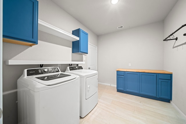 clothes washing area with visible vents, washing machine and dryer, cabinet space, and baseboards