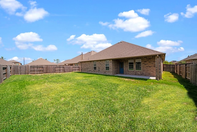 rear view of house featuring roof with shingles, brick siding, a patio, a lawn, and a fenced backyard