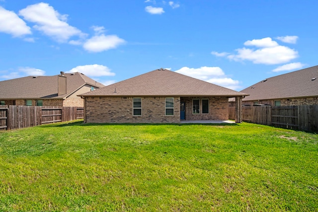 rear view of property with a fenced backyard, brick siding, a shingled roof, a lawn, and a patio area