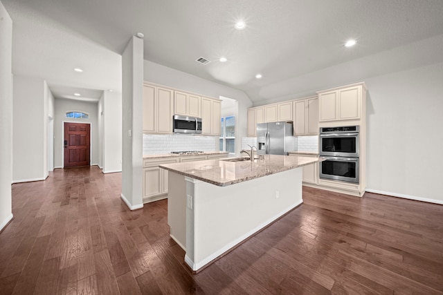 kitchen with visible vents, an island with sink, dark wood-type flooring, light stone countertops, and stainless steel appliances