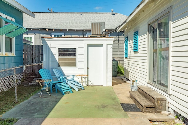 view of patio / terrace with entry steps, fence, an outdoor structure, and central AC unit