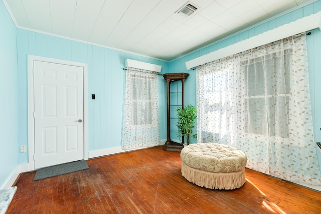 living area with wood-type flooring, visible vents, and crown molding