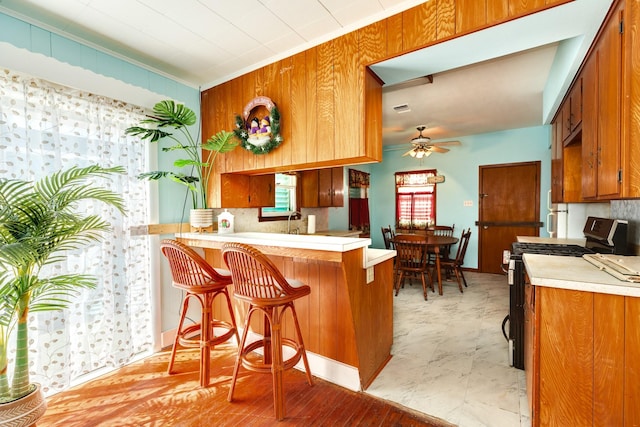 kitchen featuring brown cabinetry, gas range, a peninsula, light countertops, and backsplash