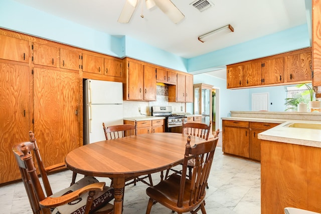 kitchen with brown cabinetry, stainless steel range with gas cooktop, freestanding refrigerator, and marble finish floor