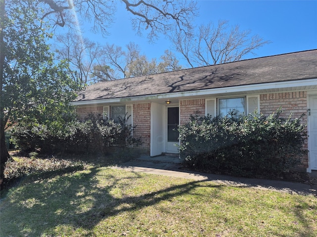 exterior space with roof with shingles, brick siding, and a front lawn