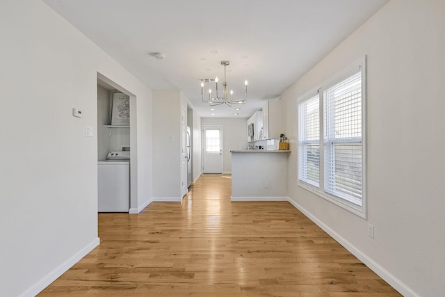 interior space with a notable chandelier, baseboards, light wood-type flooring, washer / clothes dryer, and plenty of natural light