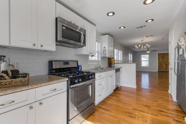 kitchen with stainless steel appliances, visible vents, light wood-style floors, white cabinetry, and tasteful backsplash