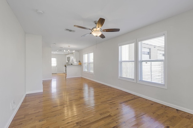 unfurnished living room featuring ceiling fan with notable chandelier, light wood finished floors, and baseboards