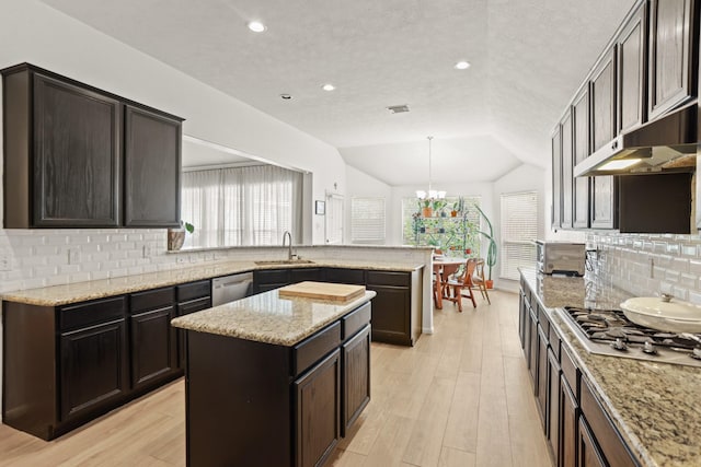 kitchen with appliances with stainless steel finishes, a peninsula, vaulted ceiling, light wood-type flooring, and a sink