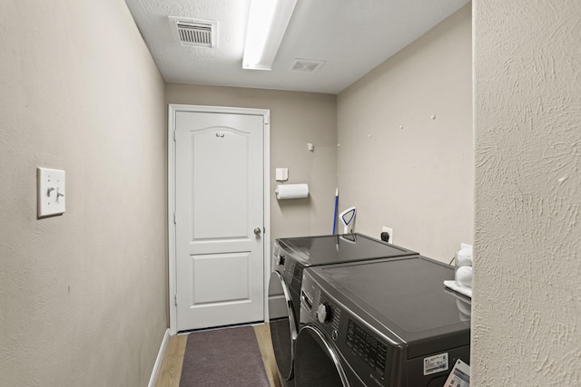 clothes washing area with laundry area, visible vents, washer and clothes dryer, and wood finished floors